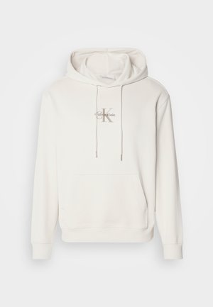 Bílá mikina s kapucí z měkké látky; má přední klokaní kapsu, žebrované manžety a logo s "Calvin Klein" nad stylizovaným "K."