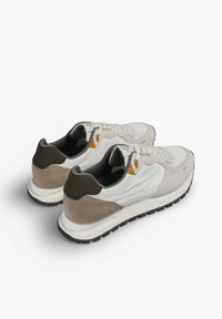 Zapatillas con una parte superior de textil blanco, acentos de ante en beige y marrón, suela texturizada negra y detalles en naranja en el lateral.