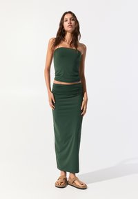 Mörkgrön, stretchig tvådelad outfit med en strapless topp och en rynkad maxikjol. Buren med bruna sandaler, slät textur.