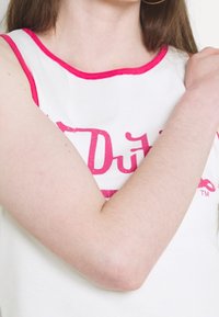 Vit linne med rosa ribbad halsringning och ärmhål, med en djärv rosa grafiktryck. Mjuk textur, avslappnad design.