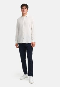 Witte lange mouwen shirt met een gemêleerde stof, knoopsluiting aan de voorkant en klassieke kraag, gecombineerd met marineblauwe broek en witte sneakers.