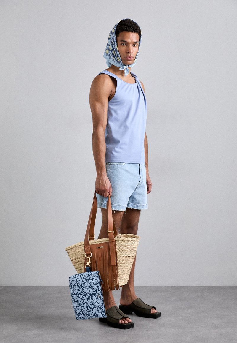 Light blue tank top, denim shorts, brown leather strap, woven straw bag with fringe, and a blue patterned pouch. Black slip-on sandals.