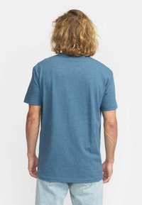 Camiseta de manga corta en tela azul jaspeada, con cuello redondo y un ajuste relajado, mostrada desde la parte trasera con dobladillo recto.