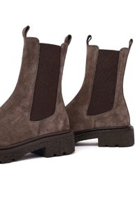 Botas Chelsea de ante marrón con paneles laterales de elástico oscuro, tiradores y una suela negra texturizada, con puntera redondeada y tacón plano.