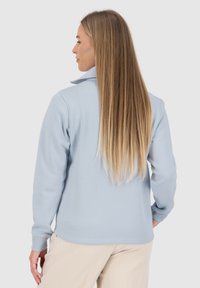 Giacca in pile azzurro chiaro con colletto alto, maniche lunghe e texture liscia, dotata di chiusura con zip e cuciture pulite.