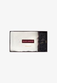 Set de máscara de sueño de pura seda y coleta para el cabello en una caja; la máscara es blanca con logotipo grabado, las coletas negras tienen detalles en dorado.