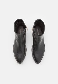 Bottes noires pour la cheville en cuir texturé avec un bout pointu, une fermeture à glissière latérale et un design minimaliste. Surface lisse et élégante.