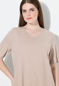 Beige V-kaula-aukollinen t-paita, valmistettu pehmeästä, kevyestä kankaasta. Lyhyet hihat, sileä pinta ja rento istuvuus. Ei näkyviä kuvioita tai logoja.