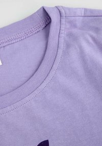 Jasnofioletowa bawełniana koszulka z okrągłym dekoltem i gładką teksturą, zbliżenie na ścieg wokół dekoltu.
