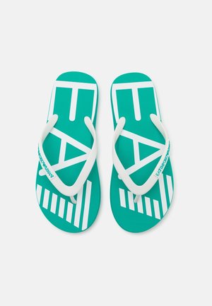 Un par de chanclas turquesa con tiras de goma blancas y un diseño gráfico de letras y líneas en la suela.