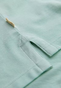 Tessuto verde chiaro con superficie texturizzata. Presenta un piccolo incavo e dettagli cuciti lungo l'orlo. Design minimalista.