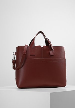 Donkerbruine leren tote bag met dubbele handvatten en een verstelbare schouderband, geplaatst op een wit voetstuk tegen een effen achtergrond.