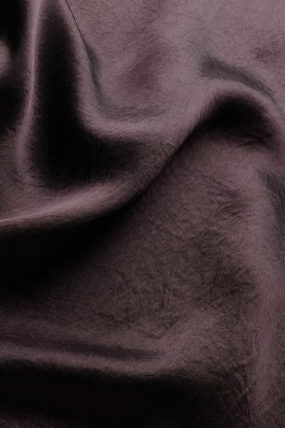 Tissu violet foncé avec des plis doux et une texture lisse, légèrement brillante sous une lumière diffuse.