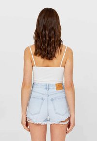 Jasnoniebieskie szorty z denimu z postrzępionym wykończeniem i jasnobrązową skórzaną metką, w połączeniu z białym prążkowanym topem na cienkich ramiączkach.