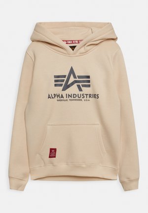 Felpa beige con logo Alpha Industries e testo "Knoxville, Tennessee, U.S.A.", tasca frontale e etichetta rossa vicino all'orlo.