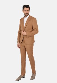 Completo marrone strutturato con vestibilità slim, giacca monopetto e pantaloni abbinati. Abbinato a una camicia bianca e mocassini grigio chiaro.