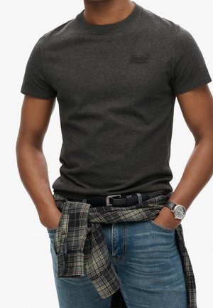 Mørk grå t-shirt med korte ærmer og rund halsudskæring, parret med bløde jeans og en ternet flannel skjorte bundet om taljen. Sølvur på håndleddet.