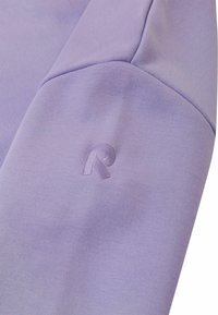 Jasnofioletowy sweter z teksturowanej tkaniny, z dyskretnym haftowanym logo w rogu rękawa.