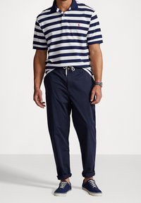 Granatowo-biała koszulka polo w paski, z krótkimi rękawami, kołnierzykiem i czerwonym logo. Do tego granatowe spodnie na sznurek oraz granatowe trampki.