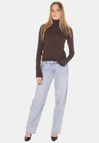 Maglione a collo alto marrone con maniche lunghe, abbinato a jeans azzurri dritti. Modella con scarpe nere con tacco alto.
