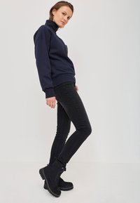 Sudor de navy din fleece cu guler înalt, asortat cu blugi negri slim-fit și cizme negre până la gleznă cu o talpă texturată.
