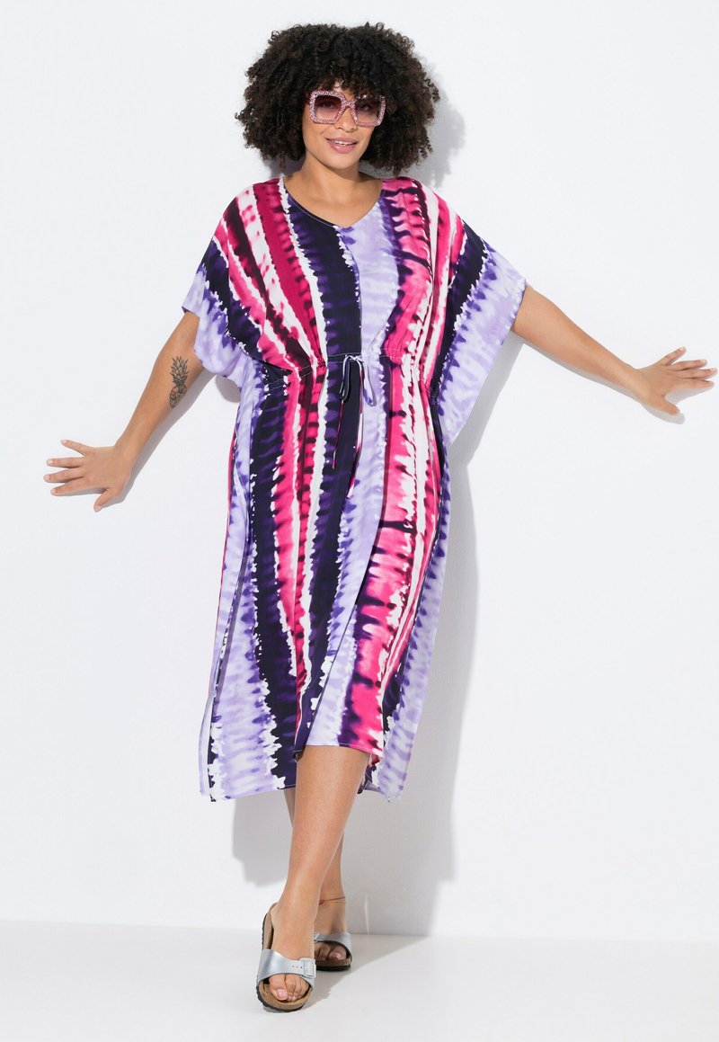 Kaftan-Kleid in lila, pink und schwarzem Batikmuster. Mit lockerer Passform, kurzen Ärmeln und einem Kordelzug in der Taille. Getragen mit silbernen Sandalen.