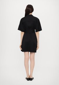 Rochie neagră cu mânecă scurtă, talie fixă, dintr-un material neted, cu croială dreaptă. Dispune de un guler clasic și o lungime până la mijlocul coapsei.