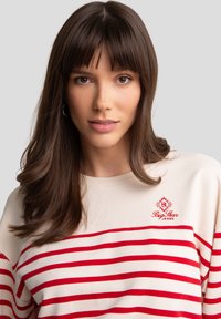 Suéter crema con rayas horizontales rojas, con escote redondo y logo bordado en el pecho. Textura suave y corte holgado.