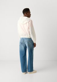 Hooded jacket with a pink to white gradient, elastic waistband, paired with wide-leg blue jeans and cream sneakers. Back view.