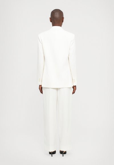 Witte op maat gemaakte blazer en wijde broek outfit. Glad materiaal, minimalistisch design en geen opvallende patronen. Zwarte hakken maken de look compleet.