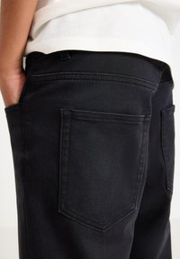 Svarta jeans i denim med en mjuk struktur, standard femfickorsdesign, synlig sömnad och en figurnära silhuett vid midjan.