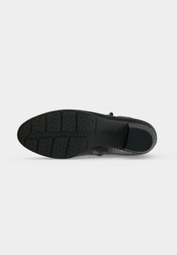 Semelle de chaussure noire avec des motifs de grip texturés et un talon bas, montrant le nom de la marque "Gabor" embossé sur la zone de la voûte plantaire.