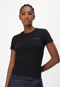 Černé tričko s krátkým rukávem vyrobené z bavlny, s kulatým výstřihem a malým bílým logem na levé části hrudníku.