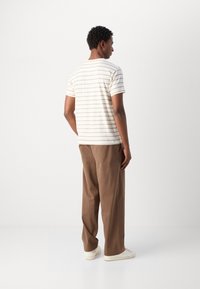 White striped t-shirt with short sleeves paired with brown loose-fitting trousers. The outfit is complemented by white sneakers.