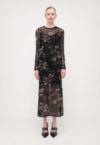 Robe noire à manches longues en tissu transparent avec un motif floral dans des tons de marron, dotée d'un corsage ajusté et d'une fente sur le côté.