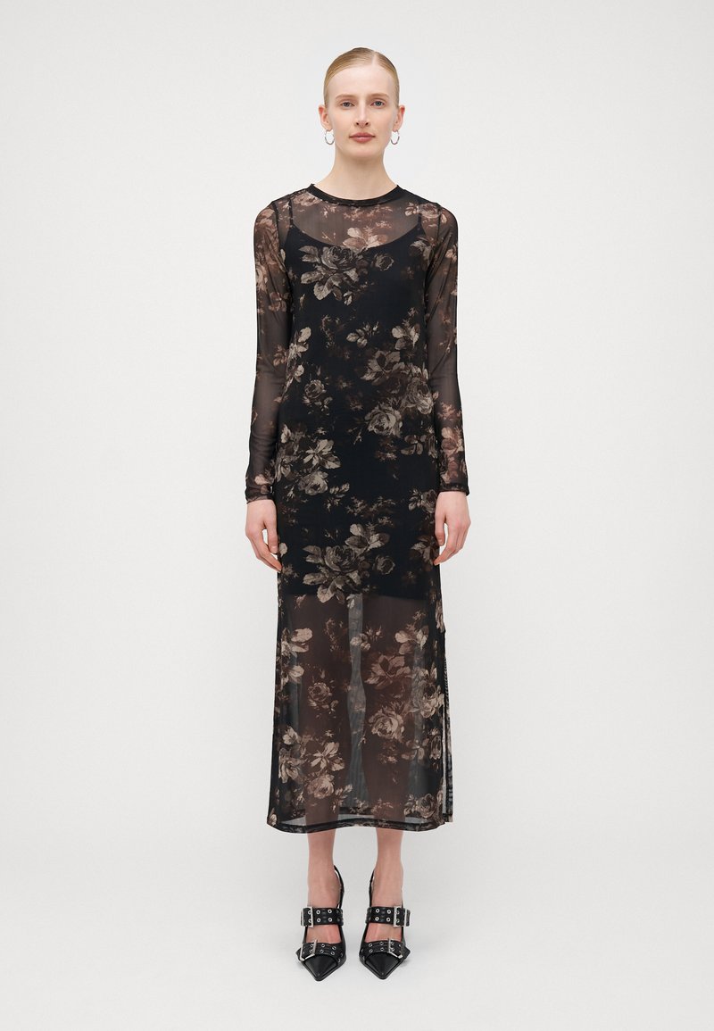 Robe noire à manches longues en tissu transparent avec un motif floral dans des tons de marron, dotée d'un corsage ajusté et d'une fente sur le côté.
