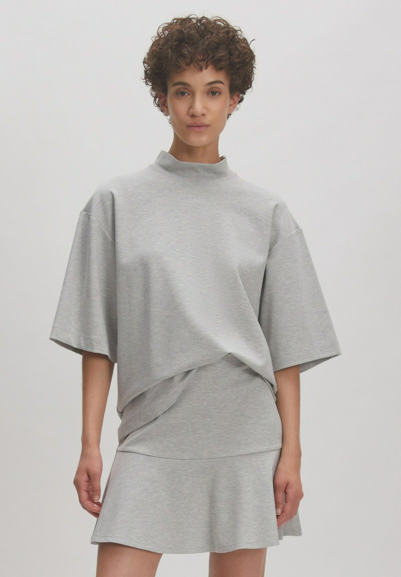 Grijze oversized top met korte mouwen, een opstaande kraag, gelaagd ontwerp en een uitlopende zoom. Soepele textuur en casual silhouet.