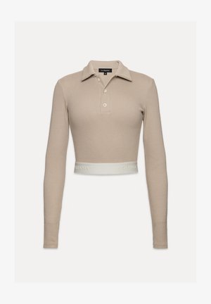 Polo stílusú, világos bézs színű, bordázott crop top, gallérral, három gombos kivágással és az alján "LA MANIA" logós fehér szalaggal.