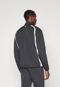 Casaco atlético preto com um colarinho alto. Apresenta riscas brancas nas laterais e um logótipo perto do pescoço. Tecido suave com um design ajustado.