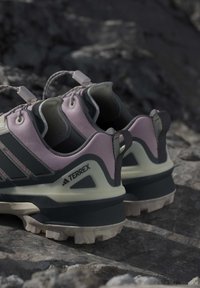 Двойка розови и черни туристически обувки Adidas Terrex върху камениста земя с дебели подметки и ушички на петите.