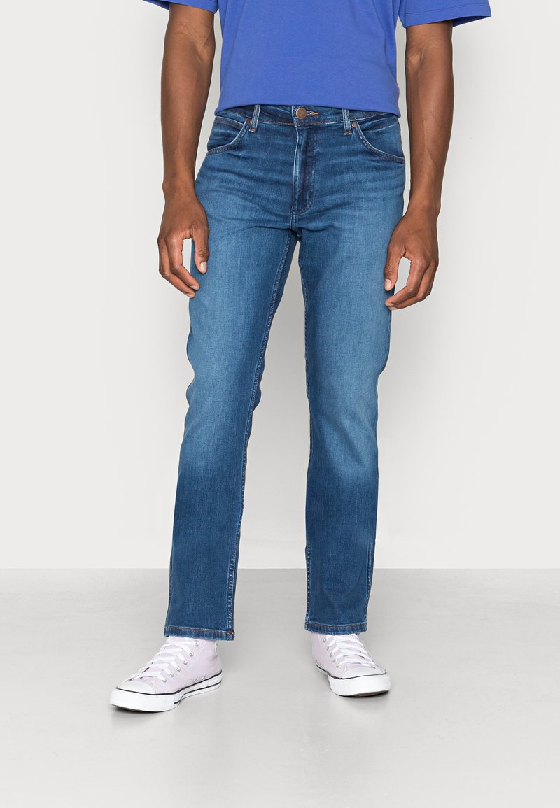 Slanke blauwe denim jeans met een klassieke vijf-pocketstijl, vervaagde textuur en een rechte pijp, gecombineerd met witte sneakers.