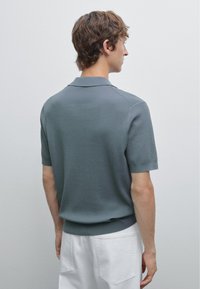 Szary prążkowany sweter typu polo z krótkimi rękawami i kołnierzykiem ze złożonym mankietem, o dopasowanym kroju i lekko teksturowanej tkaninie.