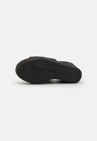 Suela negra con textura, con el nombre de la marca en relieve. Material flexible con un acento de yute natural alrededor del borde de la plantilla.