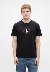 Czarny t-shirt z bawełny z okrągłym logo w czerwonym i białym kolorze oraz napisem "CALVIN KLEIN NEW YORK SINCE 1968". Okrągły dekolt i krótkie rękawy.