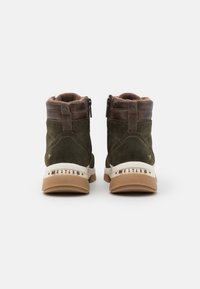 Botas de ante verdes hasta el tobillo con detalles de cuero marrón, cierre de cremallera y una suela blanca con la marca "MUSTANG".
