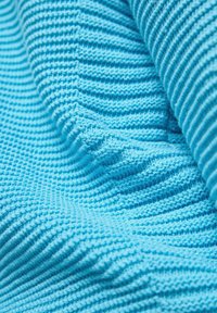 Texturiertes blaues Gewebe mit einem gerippten Strickmuster, das verschiedene Schattierungen und einen subtilen Glanz zeigt, gefaltet, um Tiefe und haptische Qualität zu verdeutlichen.