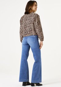 Bluse mit Leopardenmuster und gerafften Schultern, kombiniert mit hochgeschnittenen blauen Glockenjeans und schwarzen Knöchelstiefeln. Glattes Material und lockere Passform.