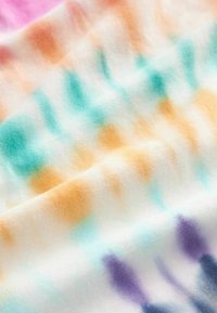 Tkanina tie-dye z białym tłem oraz wzorami w odcieniach turkusu, pomarańczy i fioletu. Miękka w dotyku z delikatnie pomarszczoną powierzchnią.