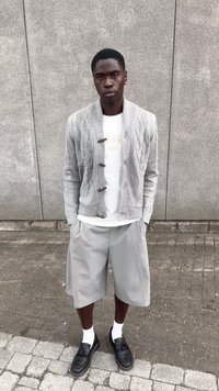 Cárdigan de punto gris claro con patrón texturizado y botones de madera oscura, combinado con pantalones cortos grises y mocasines negros. Medias blancas visibles.