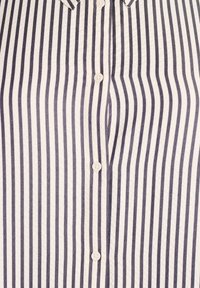 Koszula zapinana na guziki w pionowe granatowe i białe paski. Posiada kołnierzyk oraz guziki przypominające perły na przodzie. Gładka faktura materiału.